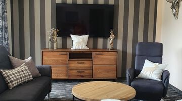 Moderner Wohnbereich mit einer Couch und einem dunkelblauen Sessel neben einem Fernseher an einer Wand