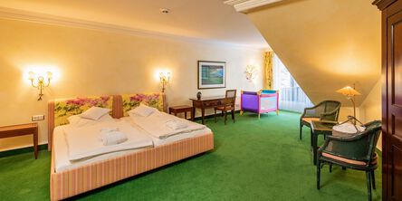 Großzügiges Doppelbett, neben einem Schreibtisch und einem Babybett auf grünem Teppichboden 