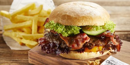 Ein saftiger Burger mit Bacon serviert auf einem Holzbrett mit Pommes.