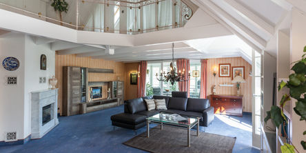 Heller Wohnbereich der Maisonette-Ferienwohnung mit einem Kamin, schwarzer Ledercouch und einem dunklem Kronleuchter