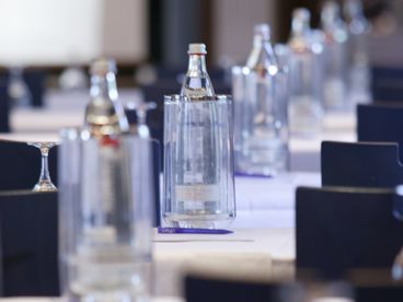 Nahaufnahme von Gläsern und Wasserflaschen auf einem langen Tagungstisch in einem Tagungsraum
