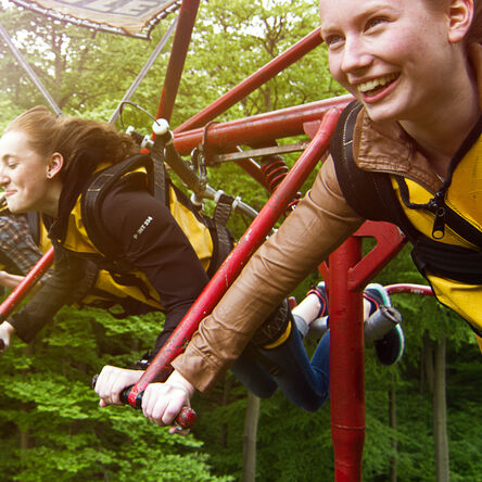 Drei Mädels fliegen in einem Fahrgeschäft durch den Wald