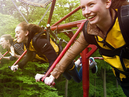 Drei Mädels fliegen in einem Fahrgeschäft durch den Wald