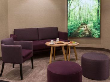 Dunkelrote Couch und Sessel an zwei hellen Beistelltischen gedeckt mit Obst und zwei Tassen 