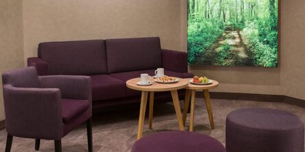 Dunkelrote Couch und Sessel an zwei hellen Beistelltischen gedeckt mit Obst und zwei Tassen 