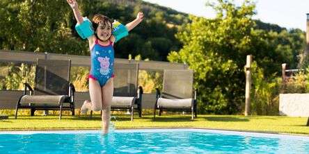 Glückliches Kind mit Schwimmflügeln springt in einen Pool im Garten
