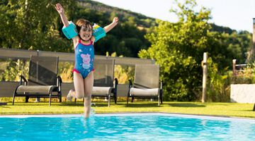 Glückliches Kind mit Schwimmflügeln springt in einen Pool im Garten