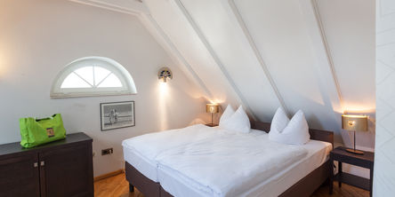 Gemütliches Doppelbett unter einer Dachschräge im Zimmer mit dunklen Holzmöbeln 