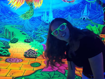 Mädchen mit einer Neonbrille im Schwarzlicht vor einem bunten Gemälde