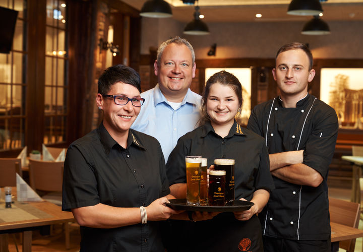 Vier Angestellte des Braushauses "Zum Löwen" posieren mit einem Tablet voller Getränke