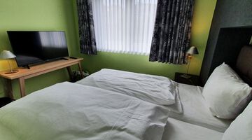 Schlafzimmer mit grünen Wänden und einem Doppelbett gegenüber eines Flachbildfernsehers