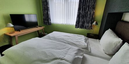 Schlafzimmer mit grünen Wänden und einem Doppelbett gegenüber eines Flachbildfernsehers