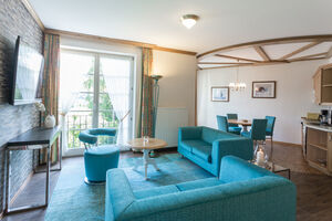 Wohnbereich mit Zugang zum Balkon, eingerichtet mit einer blauen Couch und passenden Esszimmerstühlen 
