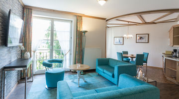 Wohnbereich mit Zugang zum Balkon, eingerichtet mit einer blauen Couch und passenden Esszimmerstühlen 