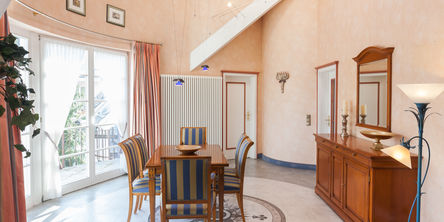 Sechs Stühle mit gesteiftem Polster an einem Holztisch in einem Raum mit hohen Decken und Zugang zum Balkon 