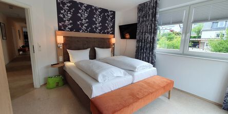 Schlafzimmer mit gemütlichem Doppelbett an einer Akzentwand mit Blumentapete neben einem Fenster mit gemusterten Vorhängen 