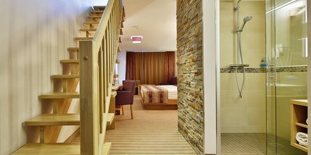 Einblick in das großzügige Doppelzmmer mit Dusche und einer Holztreppe in den zweiten Stock 
