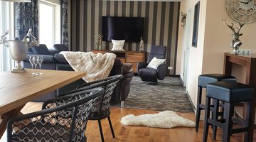 Moderner Wohnbereich mit einer Couch und einem dunkelblauen Sessel neben einem Fernseher an einer Wand