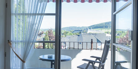 Balkon mit einem Stuhl an einem Tisch und Blick über die Stadt in die Natur 