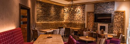 [Translate to english:] Holzvertäfelte Wände und weinrote Polstermöbel geben der Kamin-Lounge Wohlfühlcharakter
