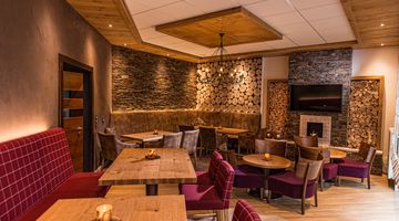 [Translate to english:] Holzvertäfelte Wände und weinrote Polstermöbel geben der Kamin-Lounge Wohlfühlcharakter