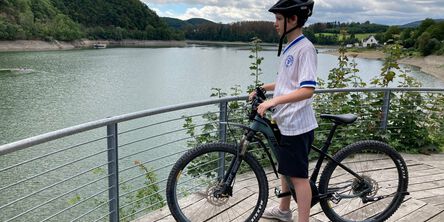 Junge steht mit seinem Fahrrad auf einer Plattform und schaut auf den See