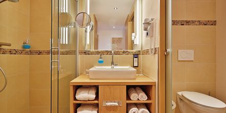 Badezimmer mit Dusche und einem Waschbecken mit gerollten Handtüchern im Unterschrank
