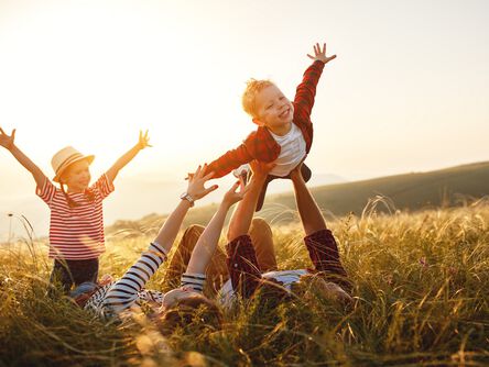 Familie liegt im Feld, der Vater spielt Flieger mit dem Sohn