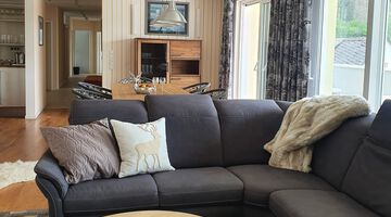 Wohn- und Essbereich des Alm Lofts mit dunkler Couch vor einem Esstisch mit vier Stühlen 