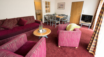 Wohnzimmer mit roter Couch und zwei passenden Sesseln auf rotem Teppichboden 