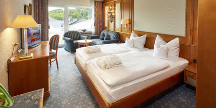 Einblick in das Zimmer mit großzügigem Doppelbett neben zwei gestreiften Sofas an einem Fenster 