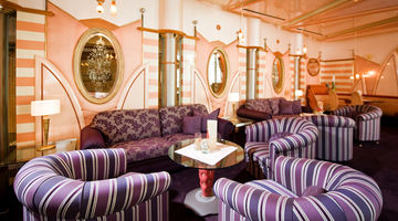Mehrere violette Polstermöbel stehen in der holzgetäfelten Lobby des Göbel Schlosshotels.