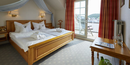 Gemütliches Doppelbett unter einem hellblauen Vorhang neben einem Balkon mit Blick über die Landschaft 