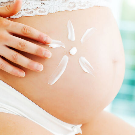 Frau malt eine Blume aus Bodylotion auf ihren schwangeren Bauch 