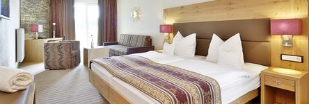 Einblick in das lichtdurchflutete Zimmer mit gemütlichem Doppelbett neben einem Sofa und einer Couch 