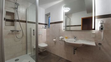 Badezimmer mit Dusche und einem beleuchteten Spiegel über dem Waschbecken neben einem Föhn 
