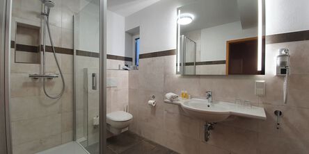 Badezimmer mit Dusche und einem beleuchteten Spiegel über dem Waschbecken neben einem Föhn 