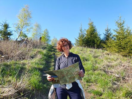 Lächelnde Frau hält eine Karte und steht auf einem Wanderweg
