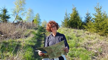 Lächelnde Frau hält eine Karte und steht auf einem Wanderweg
