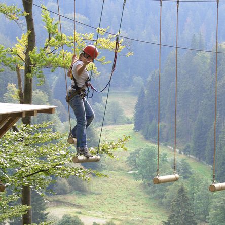 Frau klettert über Holzblöcke im Hochseilgarten 