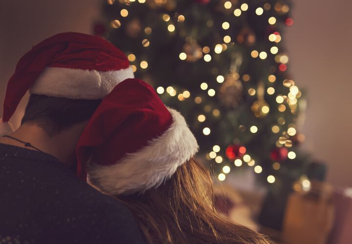 Pärchen mit Weihnachtsmützen vor einem Weihnachtsbaum