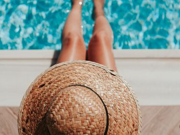 Frau mit Sonnenhut sitzt am Poolrand