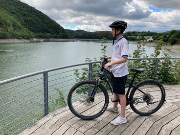 Junge steht mit seinem Fahrrad auf einer Plattform und schaut auf den See