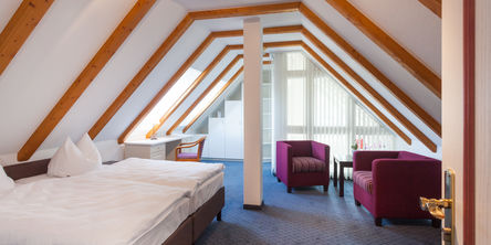 Großzügiges Doppelbett im Dachgeschoss eingerichtet mit zwei lilafarbenen Sesseln und einem Schreibtisch 