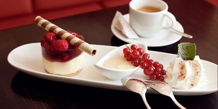 schön dekorierter Dessertteller mit Früchtetörtchen, Johannesbeeren, Sahne, daneben steht eine Kaffeetasse