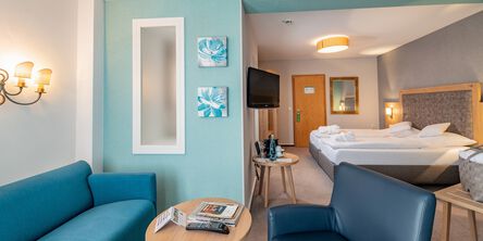 Geräumiges Schlafzimmer mit gemütlichem Doppelbett und einer Loungenische mit blauer Couch und passendem Sessel an einer türkisfarbenen Wand
