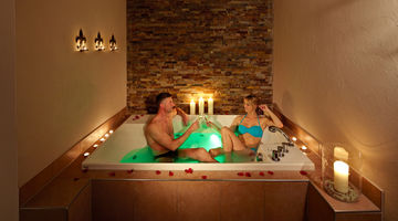 Ein Paar entspannt in einem Whirlpool des Wellnesshotels im Sauerland, der mit Rosenblättern und Kerzen dekoriert ist.