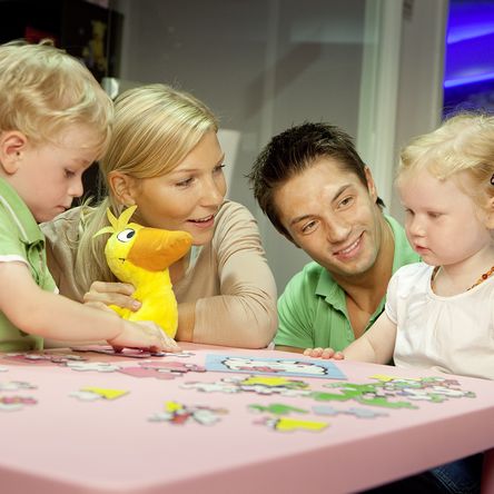 Eltern sitzen mit ihren zwei Kindern an einem Kindertisch und puzzlen 