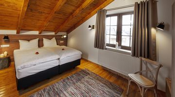 Schlafzimmer mit Doppelbett unter einer mit Holz verkleideten Dachschräge und einem Stuhl 