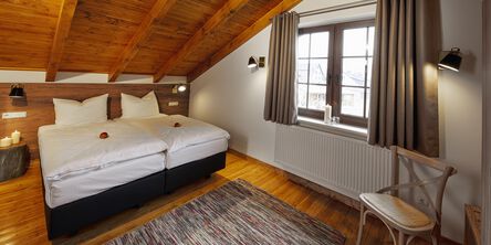 Schlafzimmer mit Doppelbett unter einer mit Holz verkleideten Dachschräge und einem Stuhl 